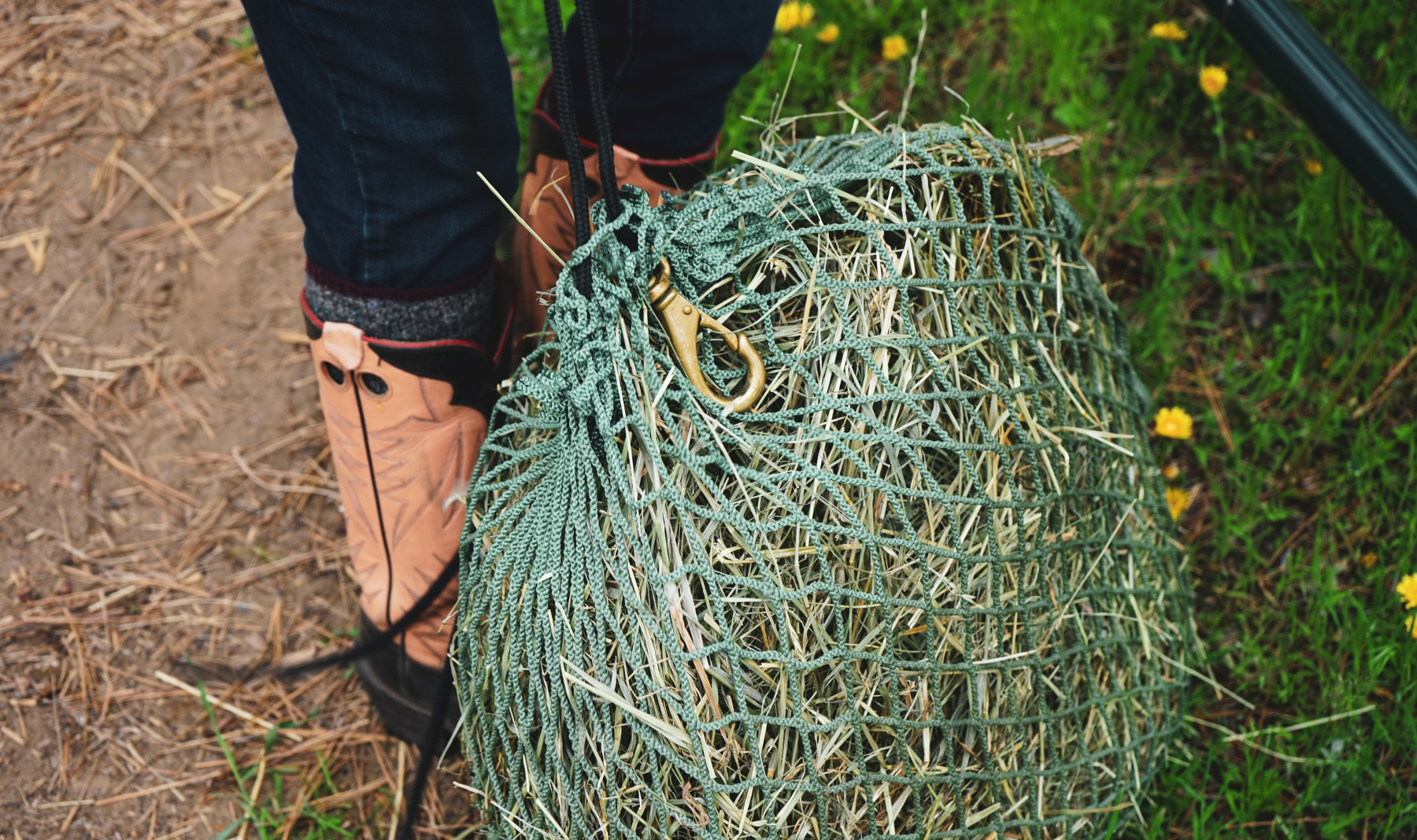 green flake feeding hay net with brass clip beside pink cowboy boots