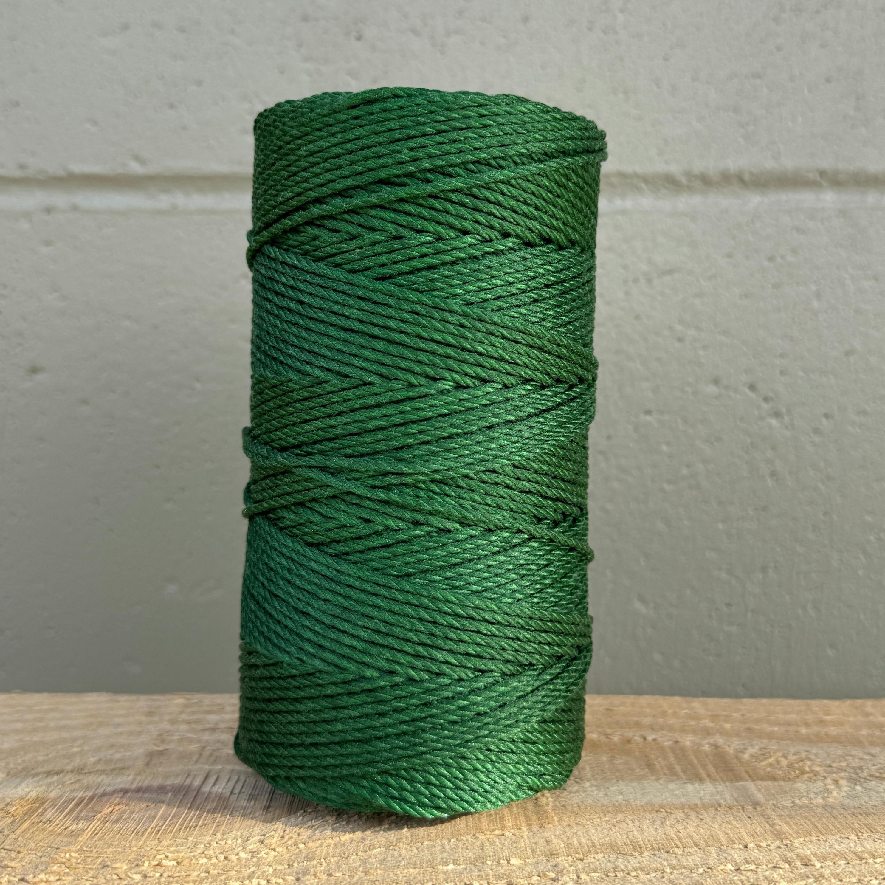 Green spool of thread on a wooden surface with a gray wall background