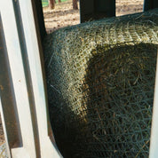 Close-up of a cylindrical net topper made of green twine, attached to a hay bale.