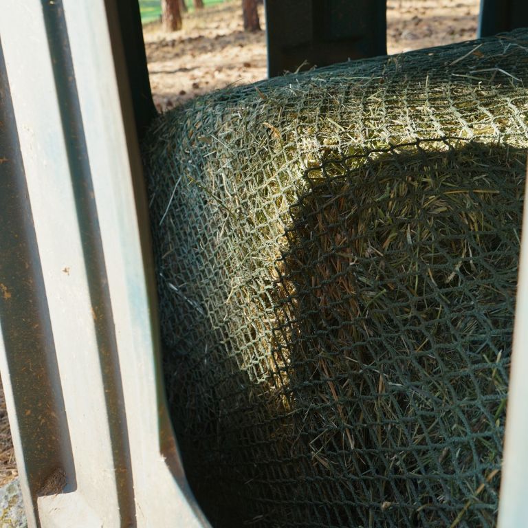 Close-up of a cylindrical net topper made of green twine, attached to a hay bale.