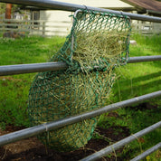 green hay net frame hanging on rail fencing 