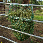 Hay net frame filled with hay attached to a metal fence in a forested area