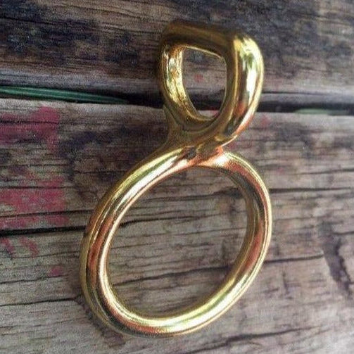 A gold-colored metal loop and ring hardware piece placed on a wooden surface.