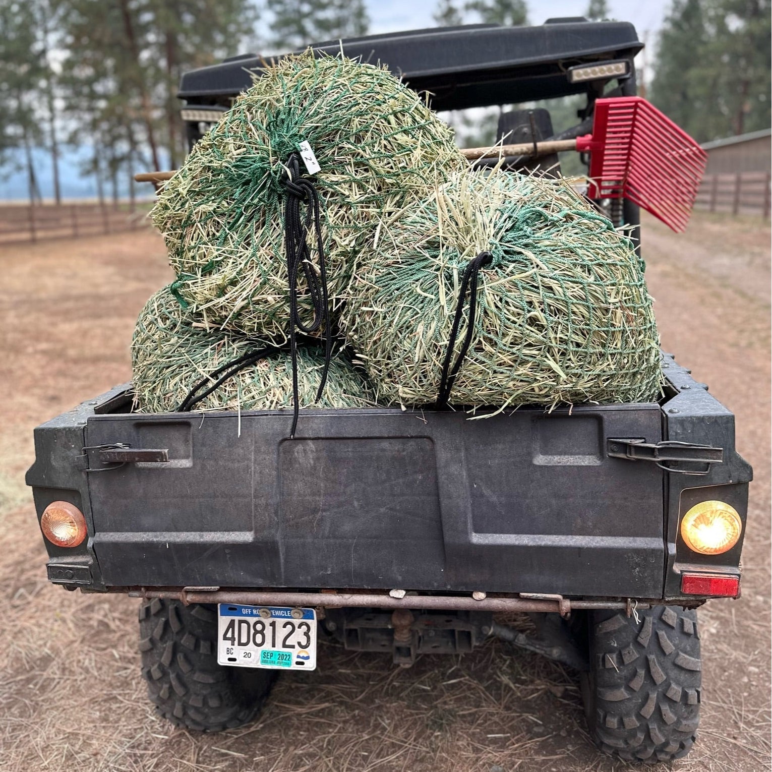 A utility vehicle with a trailer carrying bales of hay and a tied rope, set in a rural landscape.