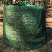 A green round bale hay net placed on the ground outdoors, likely made of nylon or polyester mesh.