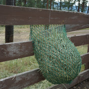 Green hay net hanging on a wooden fence with trees in the background