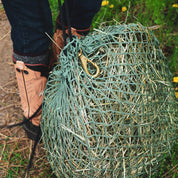 green hay net with brass clip ring on black rope with cowboy boots in the back