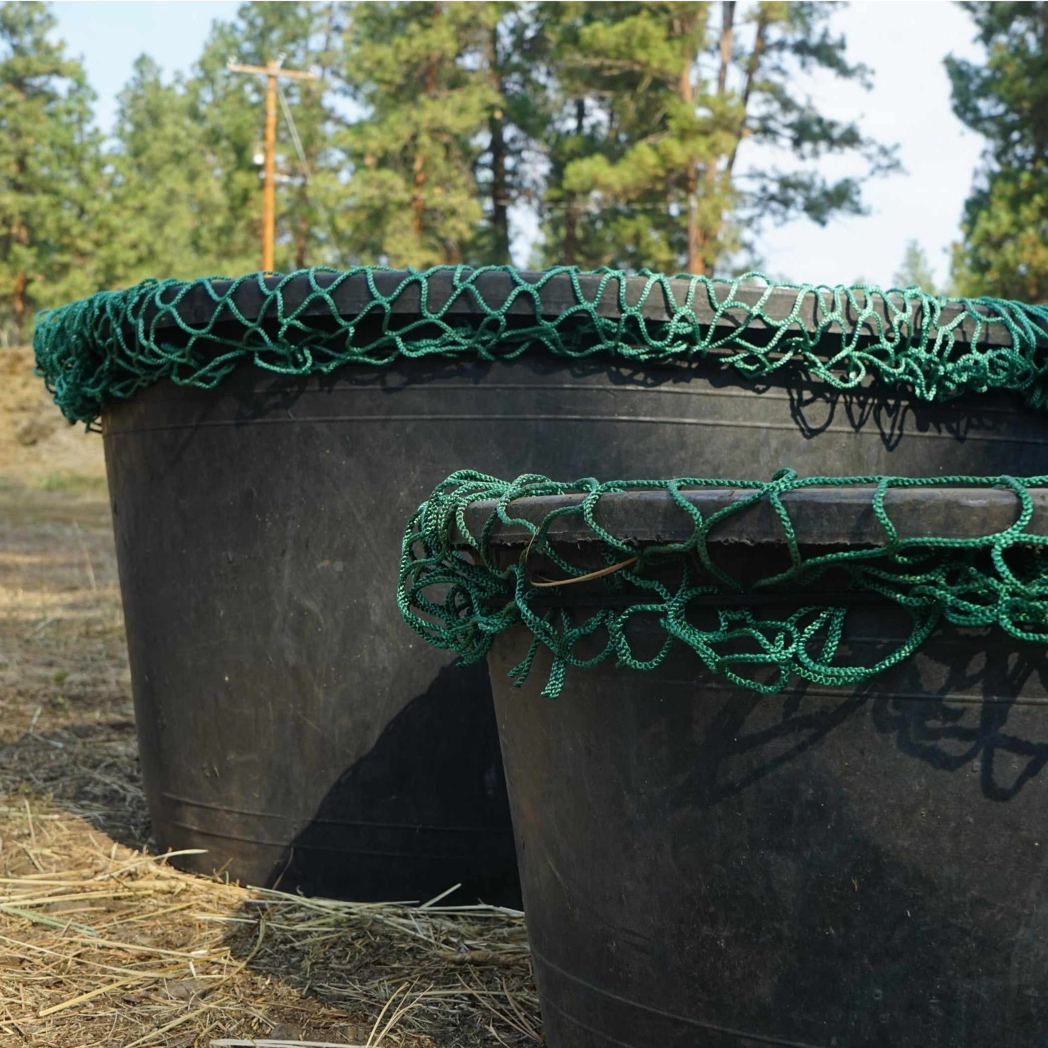 Black water tank with green netting on top in a forested area