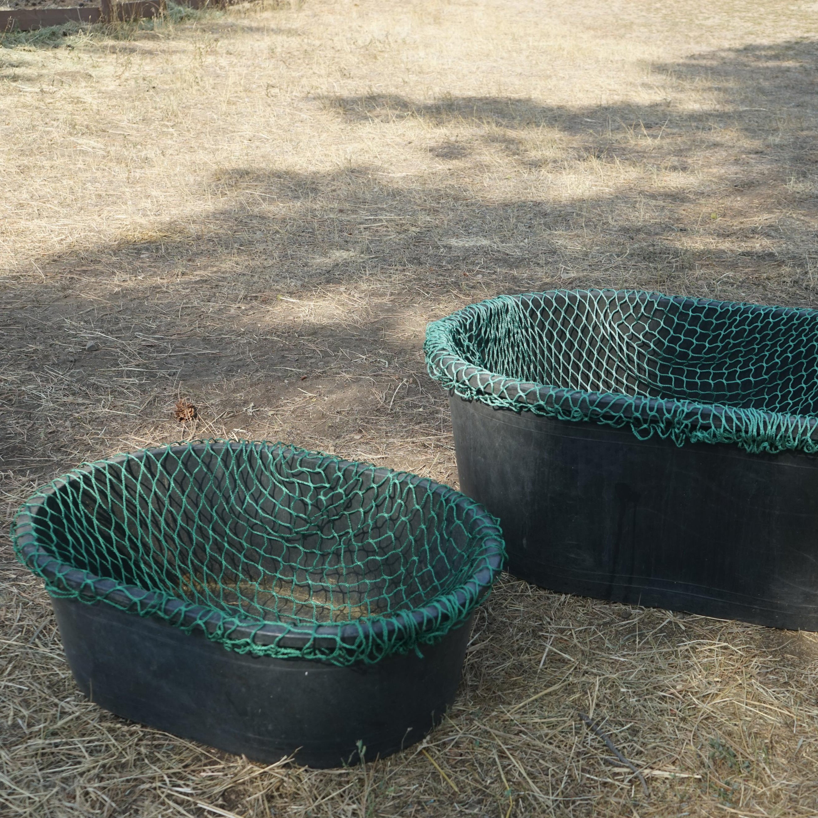 Two green and black netted containers on a dry grass surface
