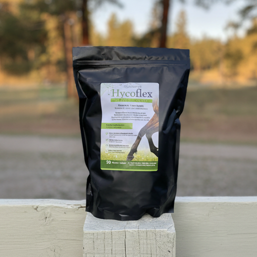 A black pouch of HycoFlex Supplement for horses placed on a wooden rail with a blurred background.